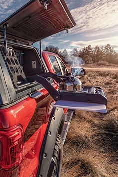 the back end of a red truck parked on top of a dry grass covered field