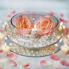 three roses in a glass bowl with pearls and candles on a floral tablecloth, surrounded by rose petals