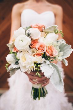 a bride holding a bouquet of white and peach flowers