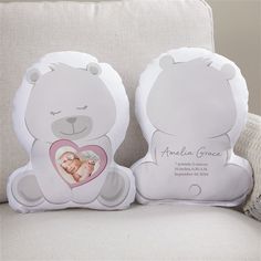 two white teddy bears holding a baby's heart shaped pillow on top of a couch