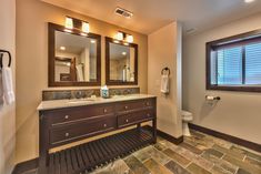 a bathroom with two sinks, mirrors and a toilet in the corner next to a window