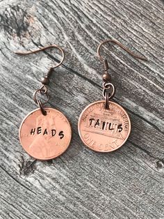 two penny earrings with the words heads and tails written on them, sitting on a wooden surface