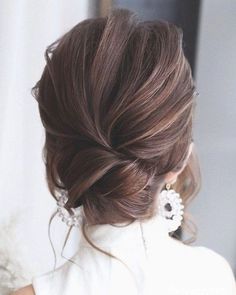 a woman with brown hair wearing earrings and a white dress is looking at herself in the mirror