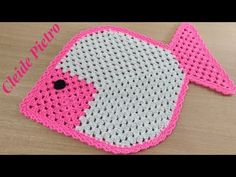 a crocheted pink and white fish on a wooden table with the words, croche