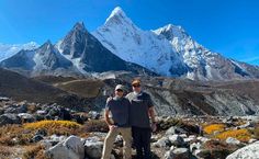 two men standing on top of a mountain with snow covered mountains in the background,