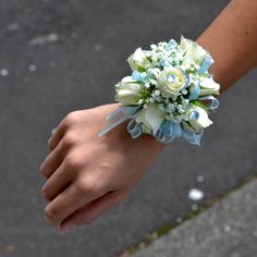 a person's hand holding a bouquet of white and blue flowers on the street