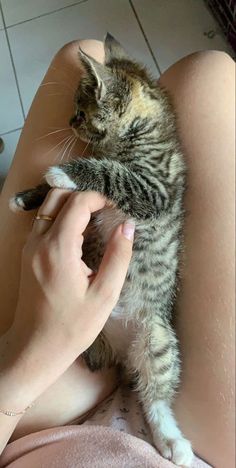 a woman is holding a kitten in her lap while laying on the floor and touching it's paw