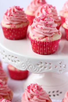 cupcakes with pink frosting and sprinkles on a white cake stand