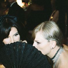 two beautiful women standing next to each other holding an open black fan in their hands