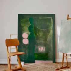 an easel sitting next to a painting on the floor in front of a chair