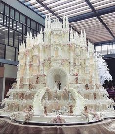 a large white cake with people standing on top of it in front of a building