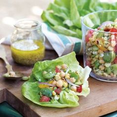 lettuce wraps filled with salad and dressing on a cutting board next to other vegetables