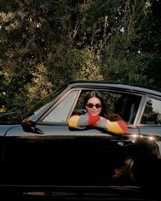 a woman sitting in the driver's seat of a black car with her arms crossed