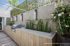 an outdoor bbq and grill area on a wooden deck next to a fenced in garden