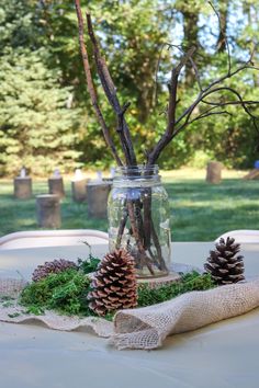 a jar filled with branches and pine cones sitting on top of a white table cloth