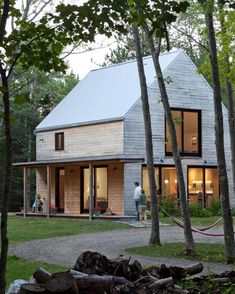 a house in the woods surrounded by trees and people standing on the front porch, looking out onto the back yard