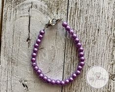 a purple beaded bracelet on a wooden surface with a silver charm hanging from the clasp