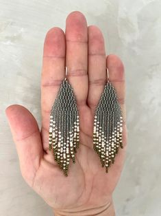 a hand holding a pair of silver and white beaded earrings on it's palm