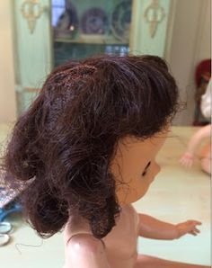 a doll with brown hair sitting on a table next to a mirror and other toys