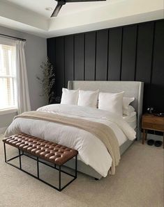 a bedroom with a large bed, white sheets and brown leather foot stools in front of the window