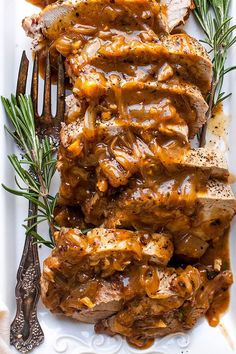 pork roast with gravy on a white platter next to rosemary sprigs