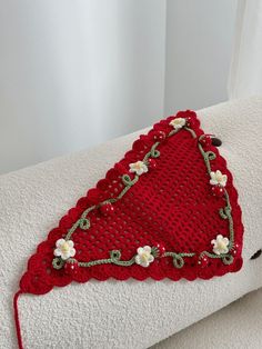 a red crocheted pillow with white flowers on it sitting on top of a bed