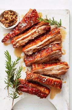 sliced pork ribs on a white platter with sauce and sprig of rosemary