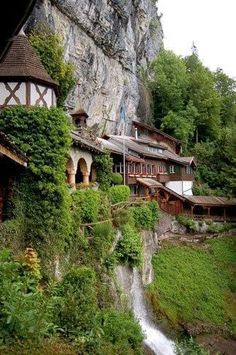 an old building with vines growing on the side of it next to a waterfall in front of a rocky cliff