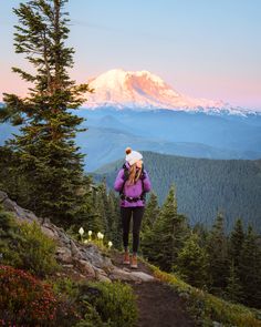 a woman standing on top of a lush green hillside next to a tall pine tree