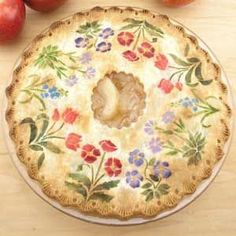 an apple pie sitting on top of a wooden table next to some apples and other fruit