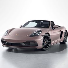 a pink porsche sports car parked in a white room with its hood up and the top down