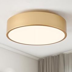 a round light fixture hanging from the ceiling in a room with white walls and curtains