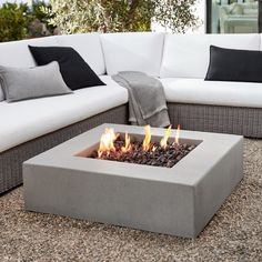 a fire pit sitting on top of a stone floor next to white couches and pillows