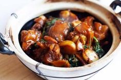 a bowl filled with meat and vegetables on top of a wooden table next to bread