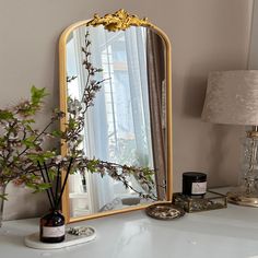 a mirror sitting on top of a white dresser next to a vase with flowers in it