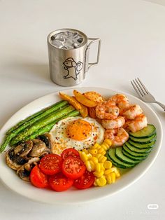 a white plate topped with veggies and shrimp next to a cup of soda