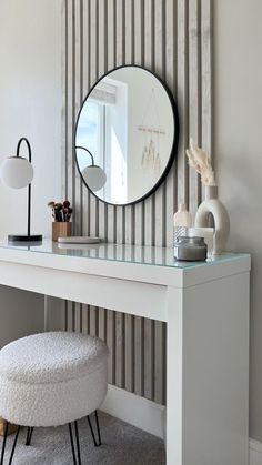 a white desk with a mirror and stool in front of striped wallpapered walls