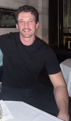 two men sitting at a table with wine glasses in front of them, smiling for the camera