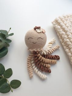 a crocheted doll sitting on top of a white table next to green leaves