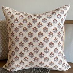 two pillows sitting on top of a wooden table next to each other, one with an orange and gray flower pattern