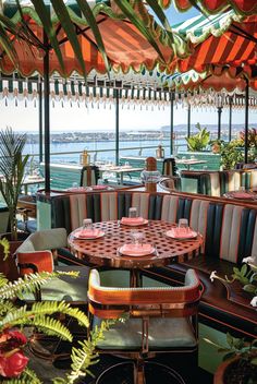 an outdoor dining area with tables and umbrellas over looking the water in front of them