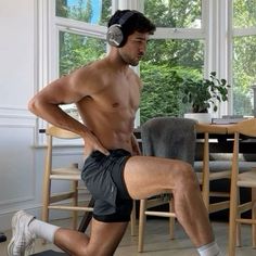 a shirtless man wearing headphones and running on a treadmill in the living room