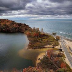 an aerial view of a lake and road in the fall with storm clouds above it