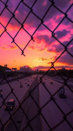 the sun is setting over an interstate with cars driving down it's lane in front of a cityscape