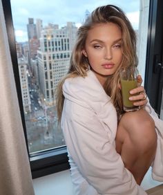 a woman is holding a glass in front of a window and looking at the camera