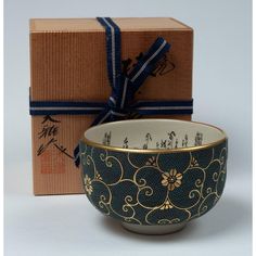 a black and gold decorated bowl sitting in front of a box with a blue ribbon