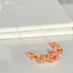 These Handmade Beads resemble candy corn with their swirl of orange and yellow glass encapsulated within each clear drop. These gorgeous beads are individually handcrafted by highly skilled glassblowers who make them by manipulating molten glass in the fiery embrace of a torch.  This process is called lampworking. Unicorne Beads are created from "hard" or borosilicate glass. Only the finest imported glass from Europe and the United States is used. Many of the colored glass is custom mixed. Boros Silver Beaded Necklace, Necklace Orange, Glass Bubble, Bubble Necklaces, Silver Bead Necklace, Teardrop Necklace, Orange And Yellow, Handmade Beads, Adjustable Necklace