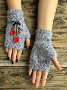 a woman's hands wearing gray knitted gloves with red flowers on them