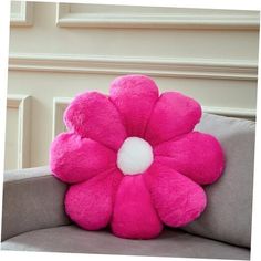 a pink flower pillow sitting on top of a gray couch next to a white wall