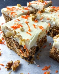 carrot cake with white frosting and orange sprinkles cut into squares on a piece of parchment paper